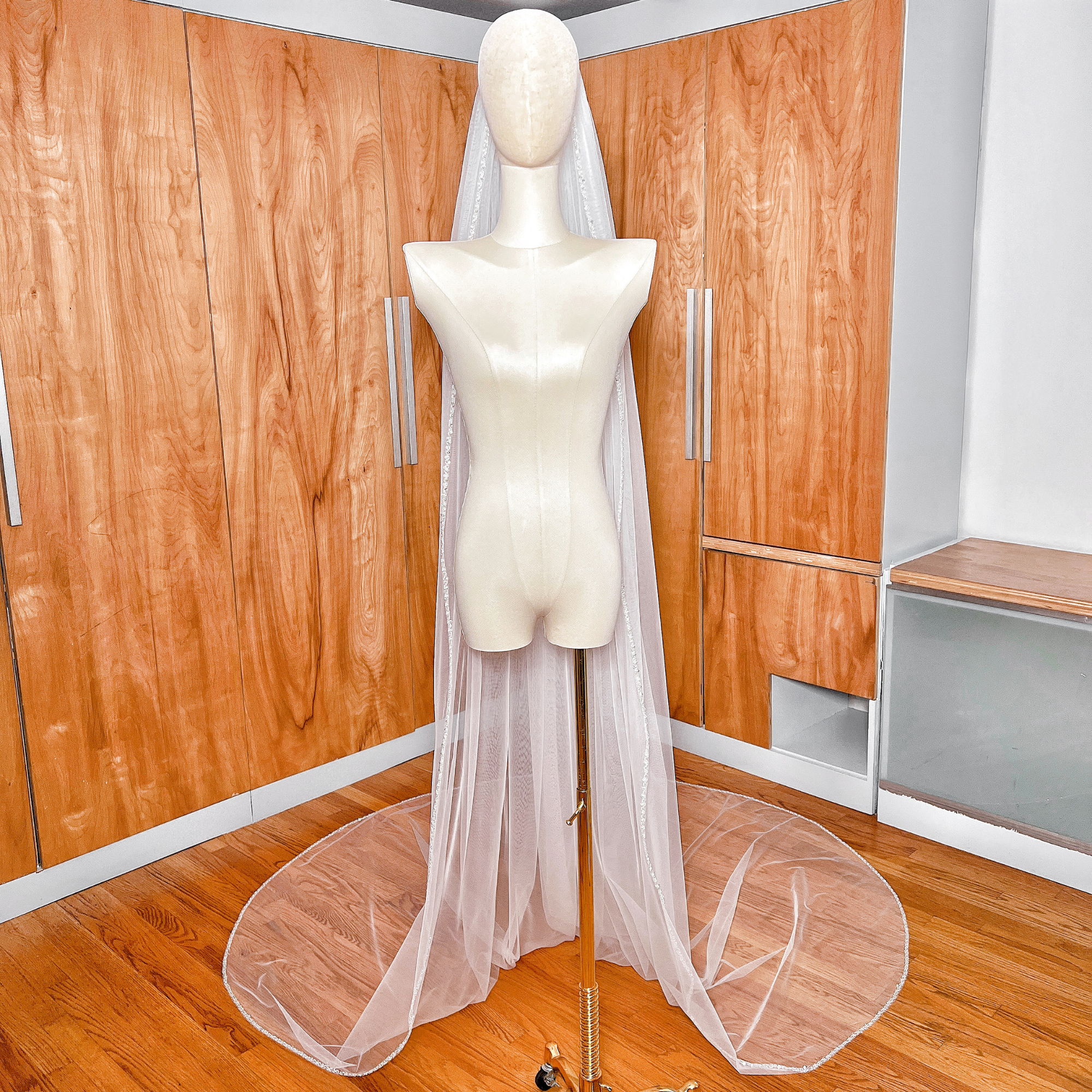 Dramatic drape of a wide cathedral length bridal veil with elegant pearl accents along the hem.