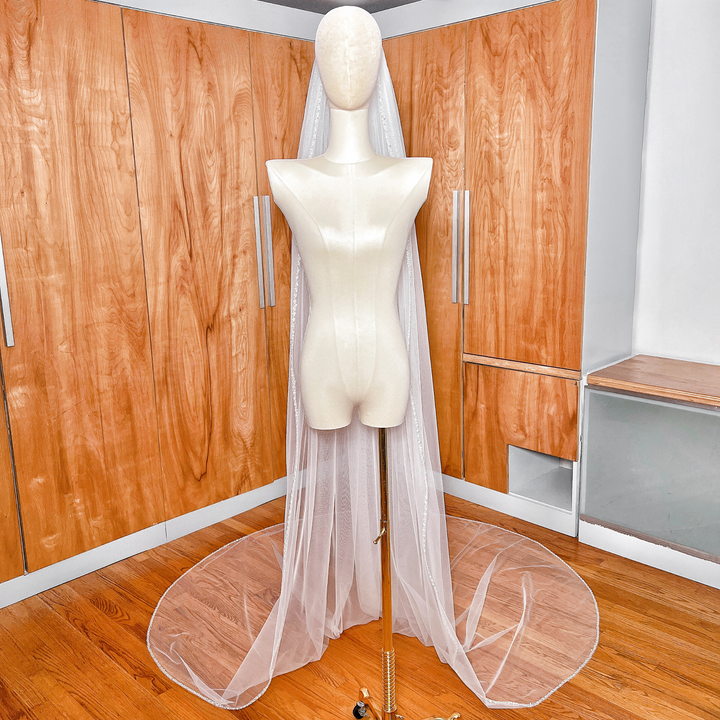 Dramatic drape of a wide cathedral length bridal veil with elegant pearl accents along the hem.