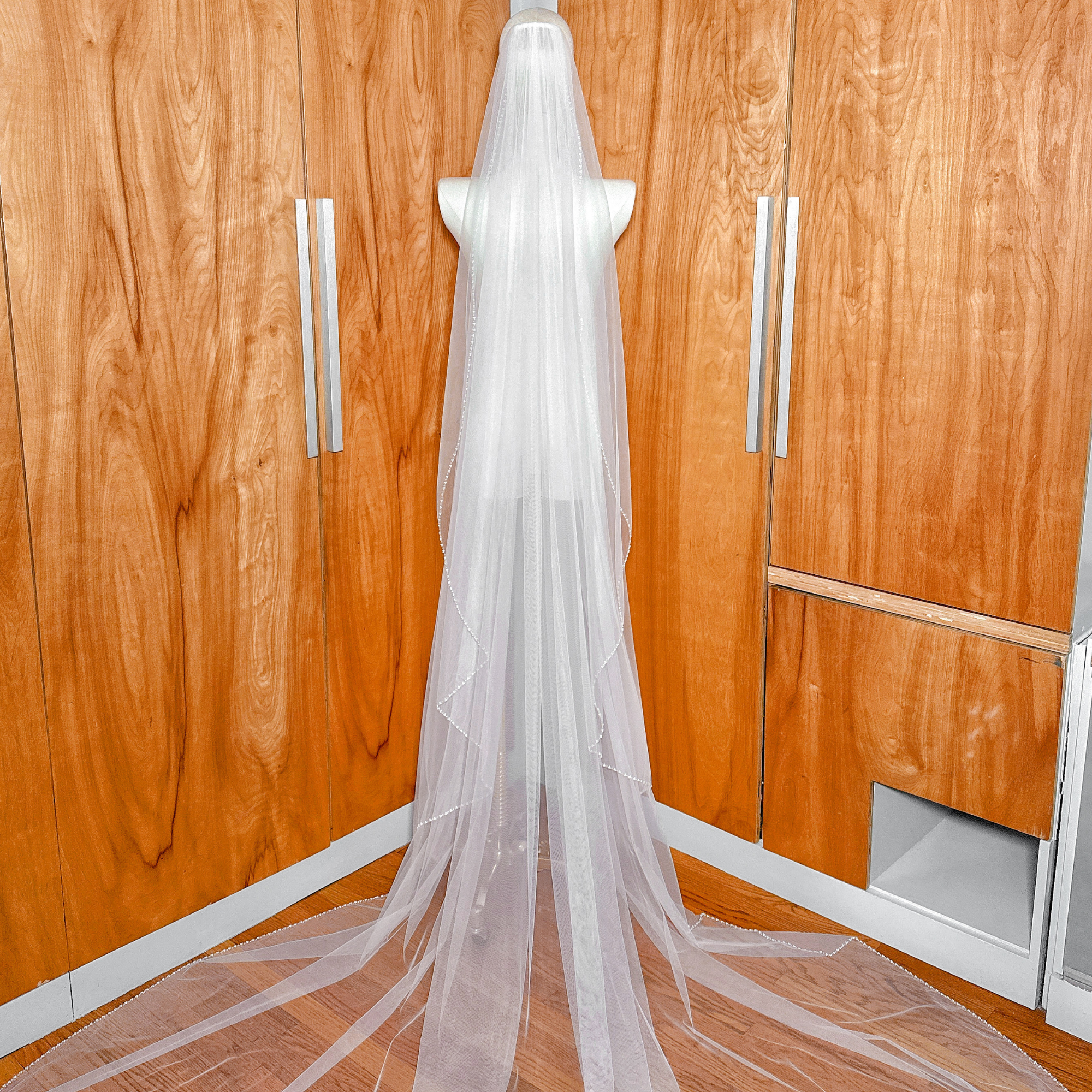 Full-length display of a luxury cathedral length cascade wedding veil featuring a hand-beaded edge.