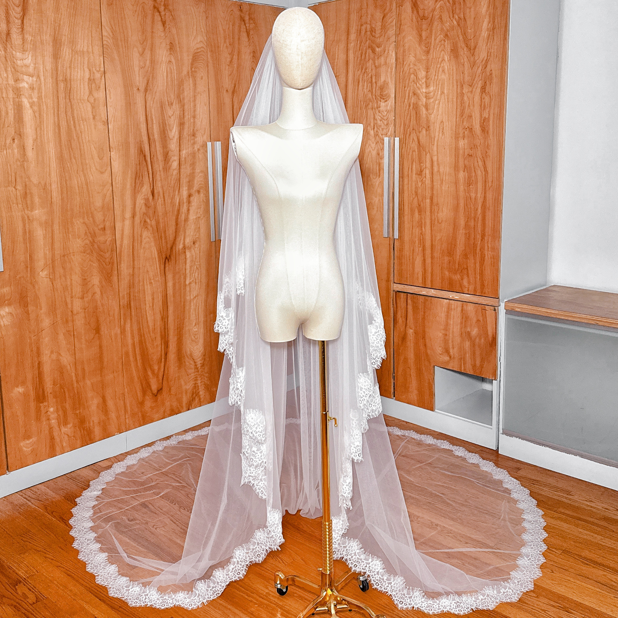 A wide shot of a luxury Two Tier Chantilly Lace Wedding Veil in cathedral length trailing behind a mannequin.