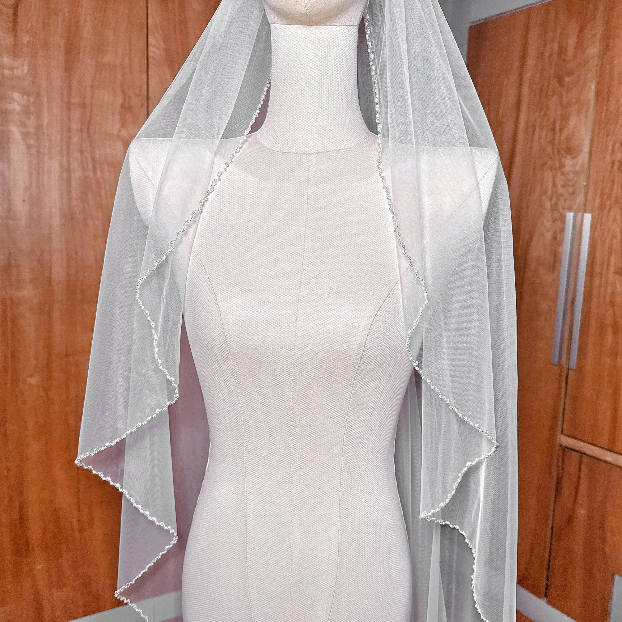 Detailed view of the pearl trim craftsmanship on a sheer angel cut cathedral bridal veil.