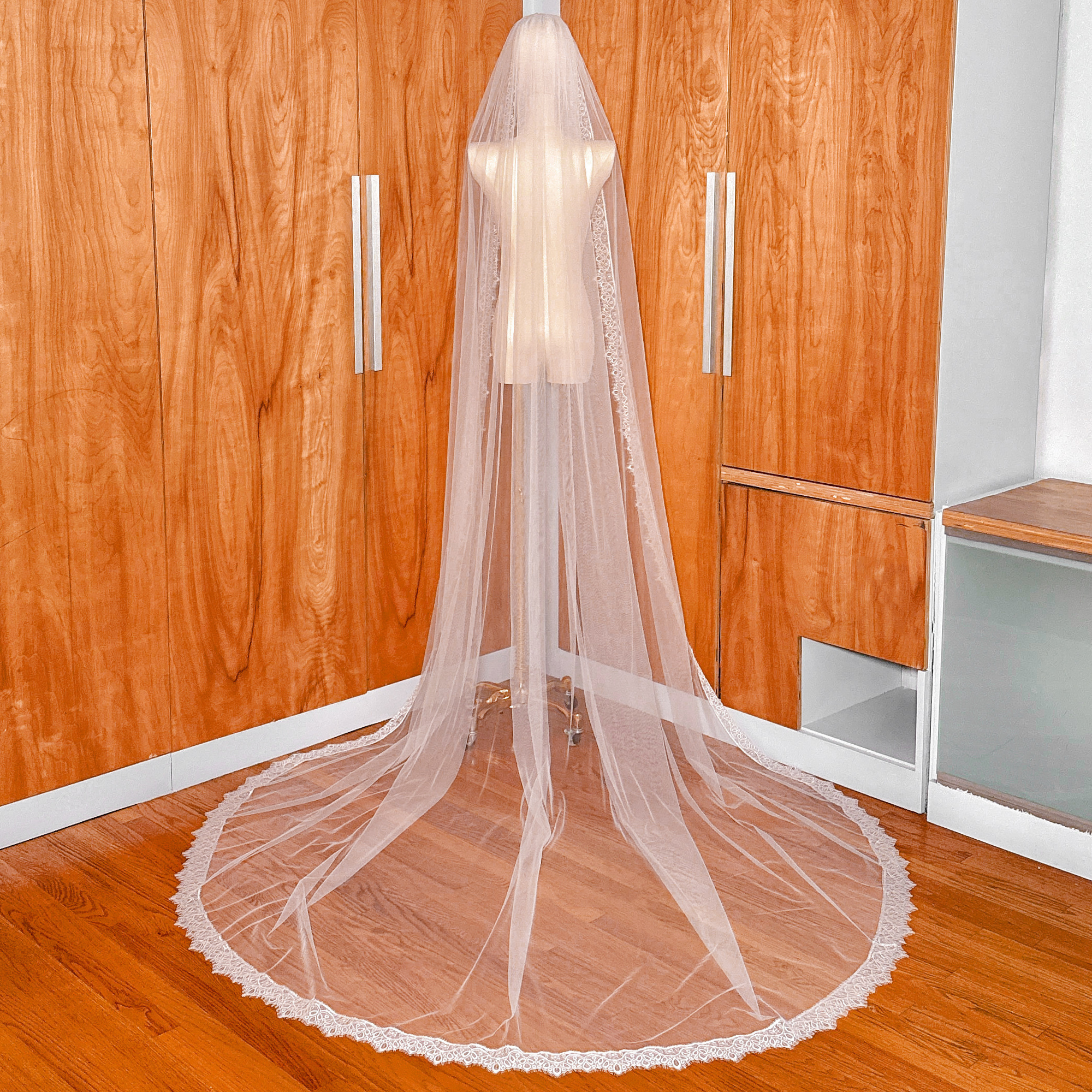 Luxurious cathedral length Chantilly lace veil with a fine net background on a mannequin.