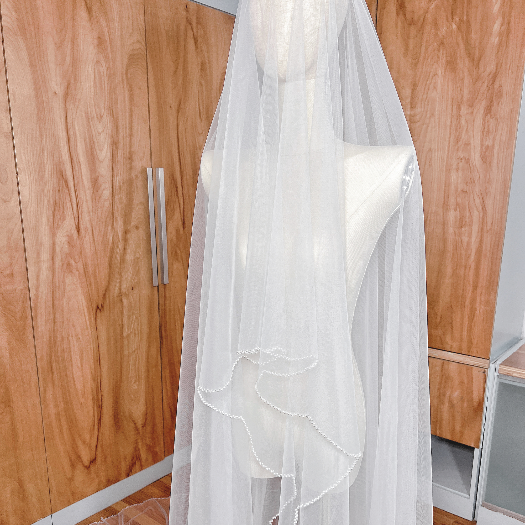Elegant cathedral length wedding veil with two tiers and pearl trim, shown draped on a bridal form.
