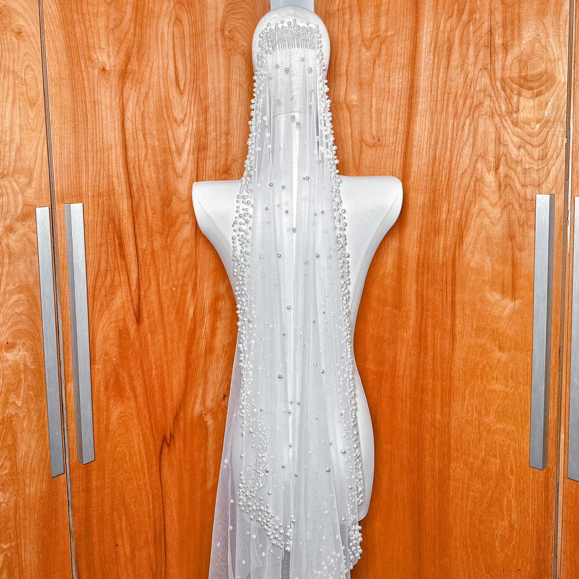 Elegant cathedral length mantilla wedding veil with scattered pearl edges draped over a mannequin for a dramatic bridal look.