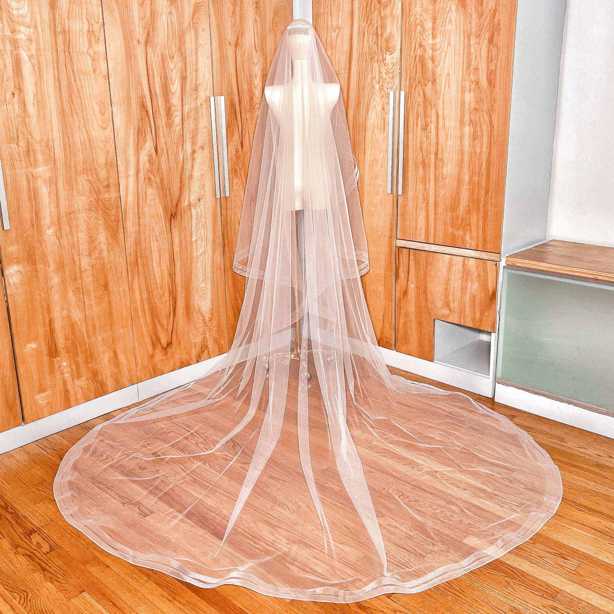 Full-length view of a luxury two tier cathedral veil with double horsehair trim flowing from a mannequin.