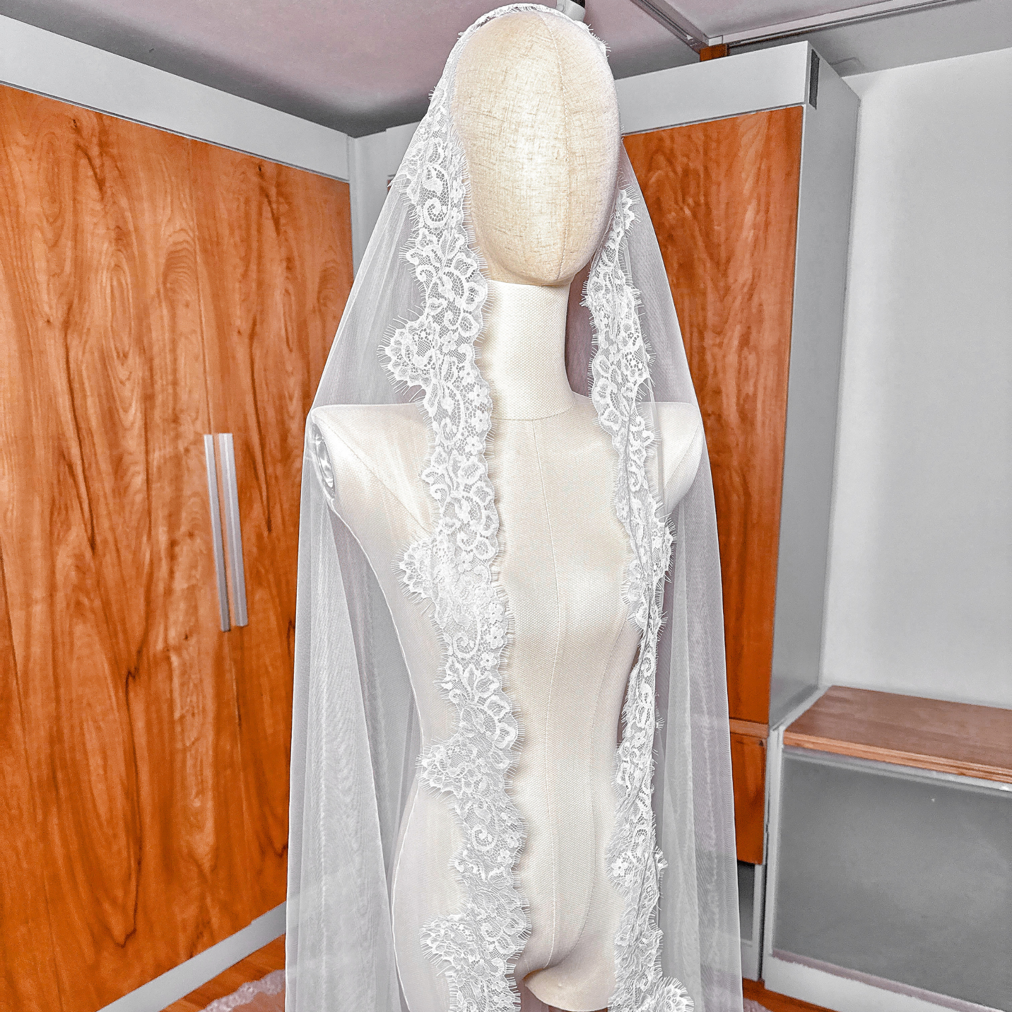 Cathedral length Chantilly lace mantilla wedding veil draped gracefully on a mannequin to display the romantic floral pattern.