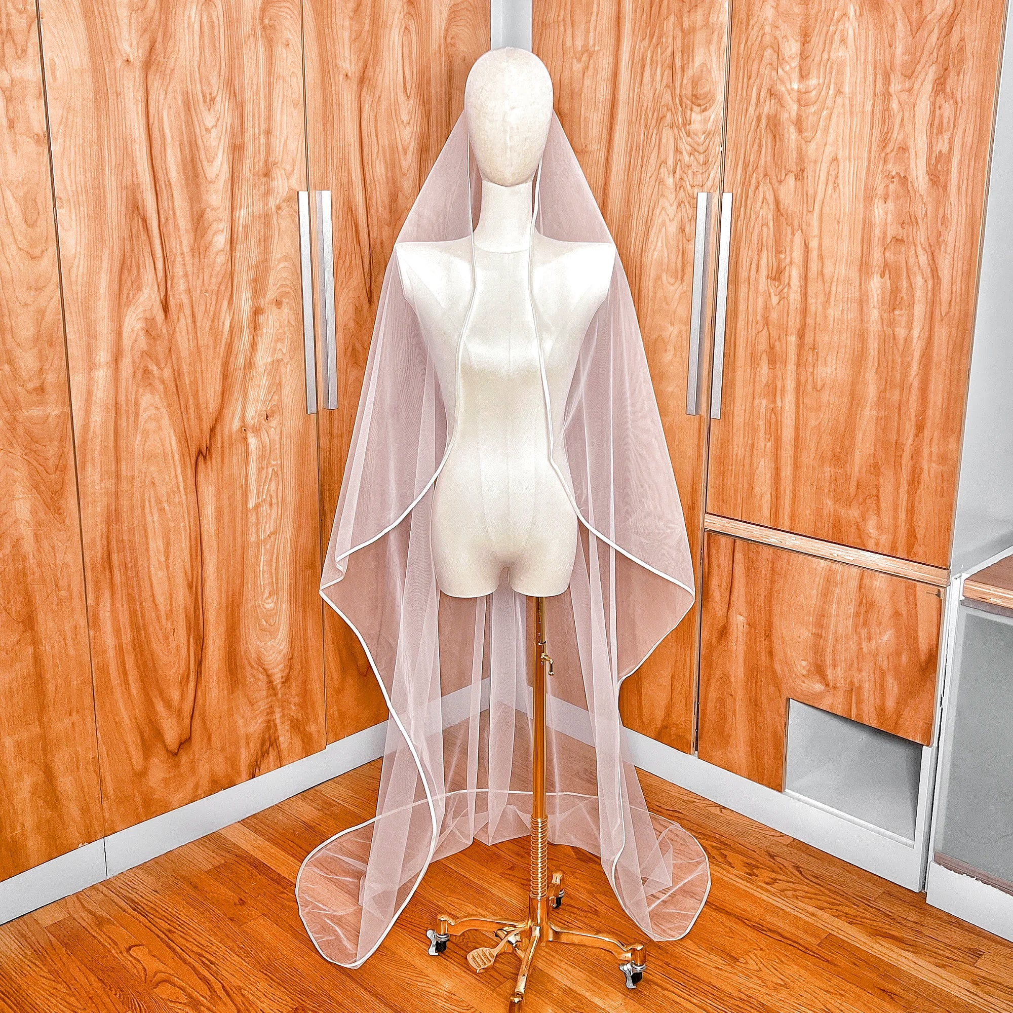 Front view of a white mantilla wedding veil with satin ribbon trim displayed on a bridal mannequin.