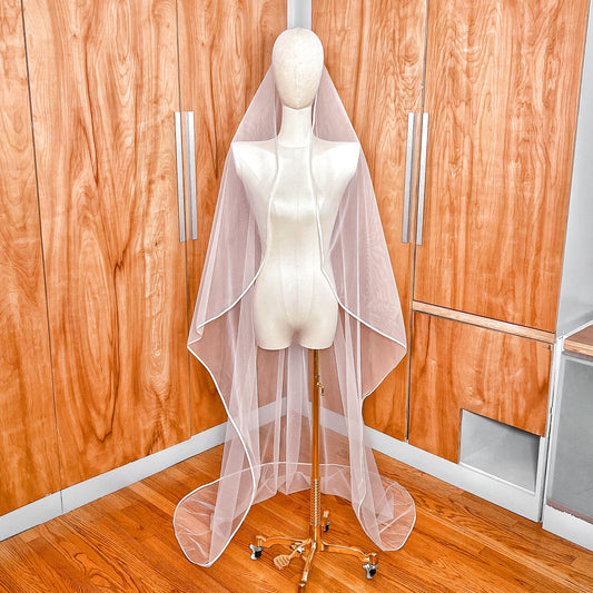 Front view of a white mantilla wedding veil with satin ribbon trim displayed on a bridal mannequin.