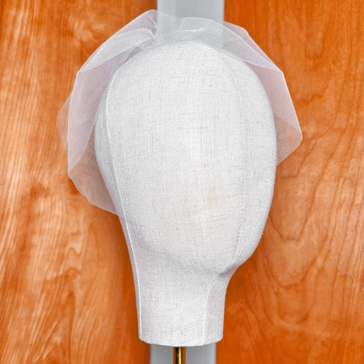 Front view of a short blusher-style mini tulle birdcage wedding veil demonstrating the sheer facial coverage and structure.