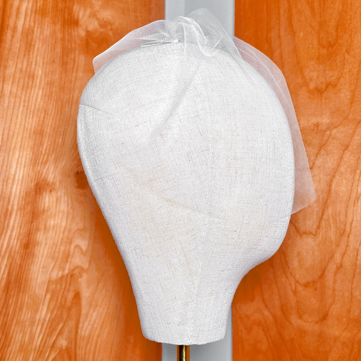Close-up of an ivory mini tulle birdcage wedding veil displayed on a bridal bust showcasing the delicate mesh netting pattern.