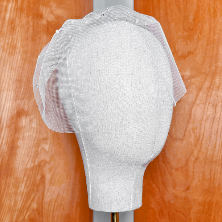 Angled view showing the shape of a mini tulle birdcage wedding veil with rhinestones and pearls.