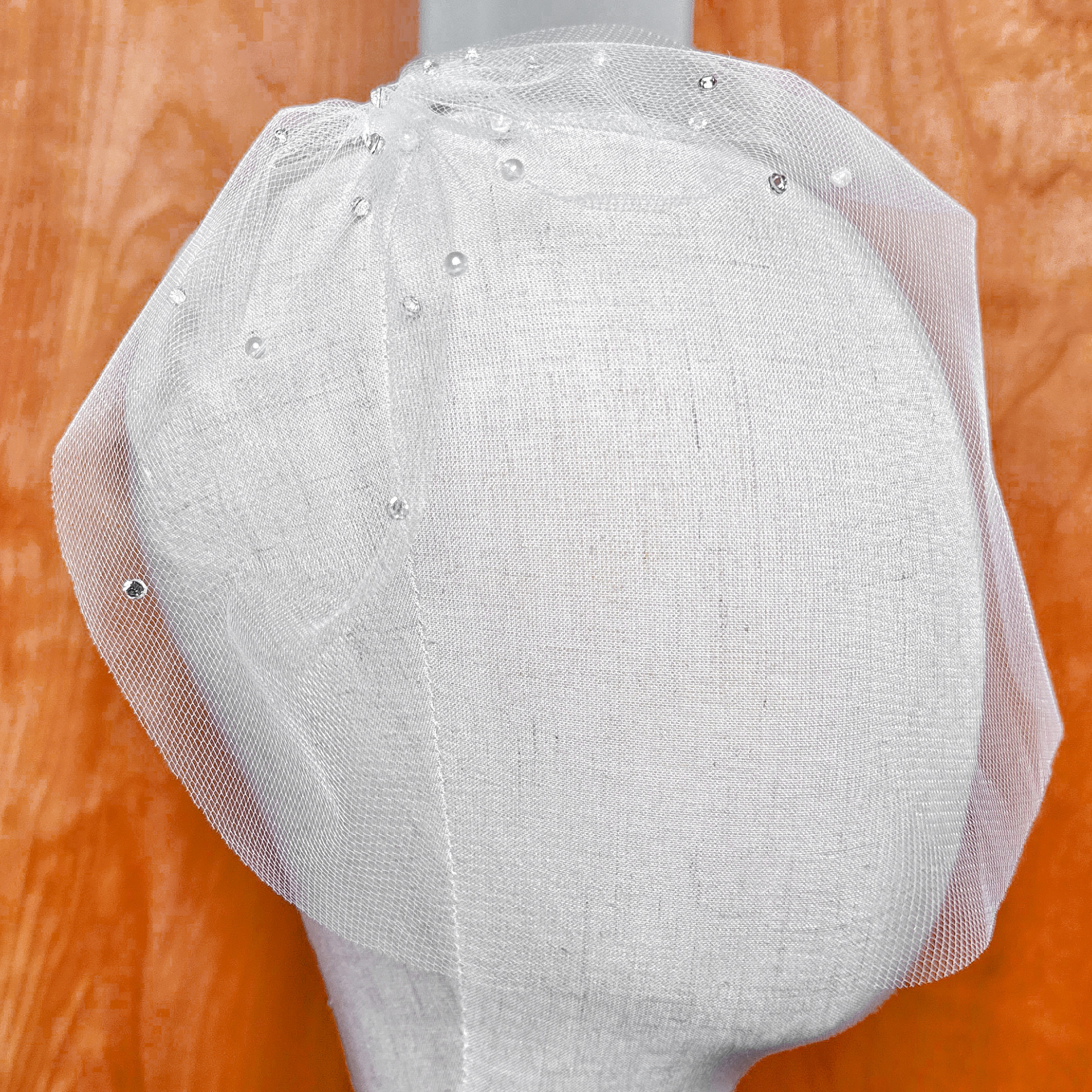 Close up view of a mini tulle birdcage wedding veil with rhinestones and pearls.