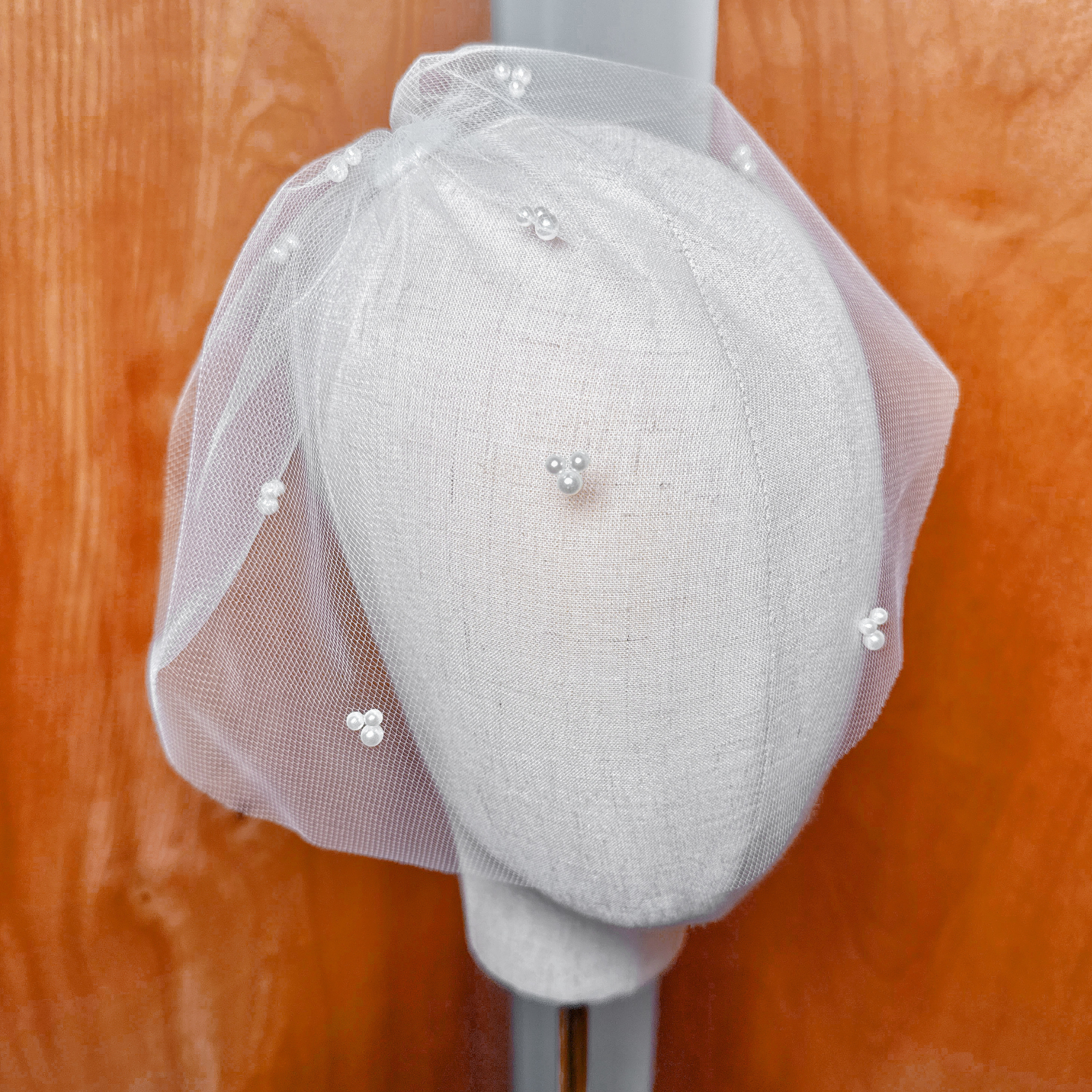 Macro close-up of the delicate white netting and cluster pearls on the mini tulle birdcage wedding veil.