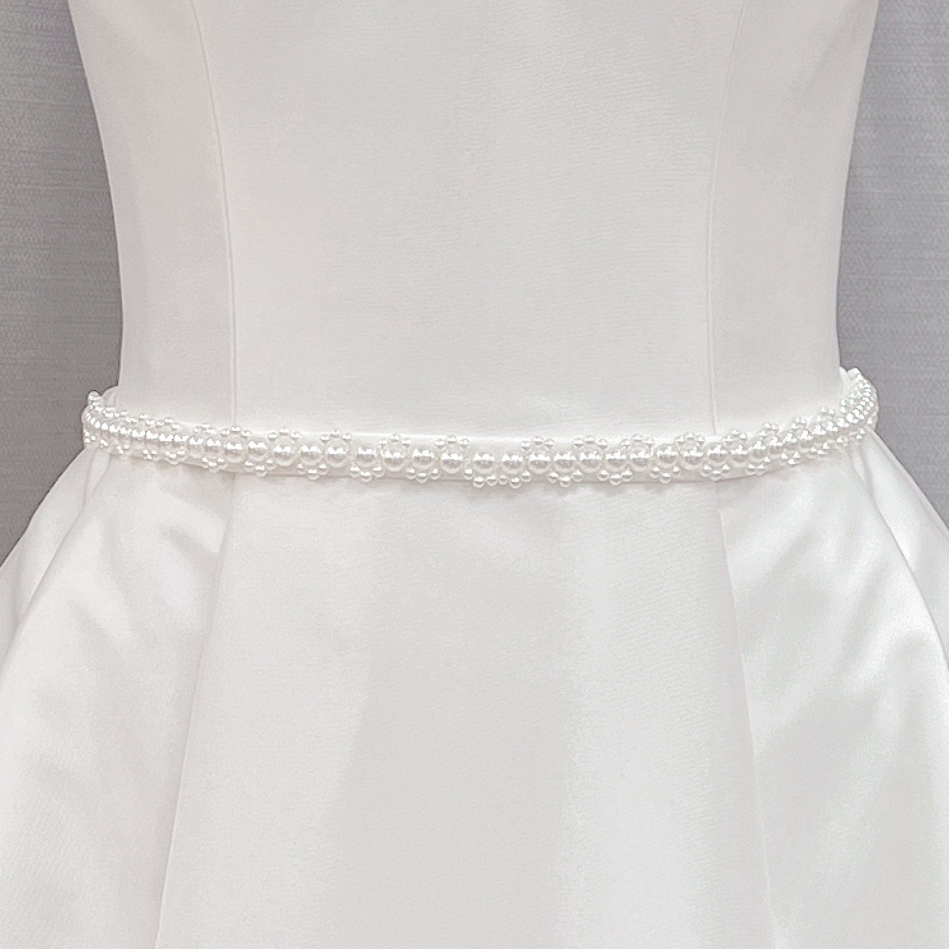 Minimalist pearl bridal belt with delicate white pearls displayed on a white bridal gown fabric background.