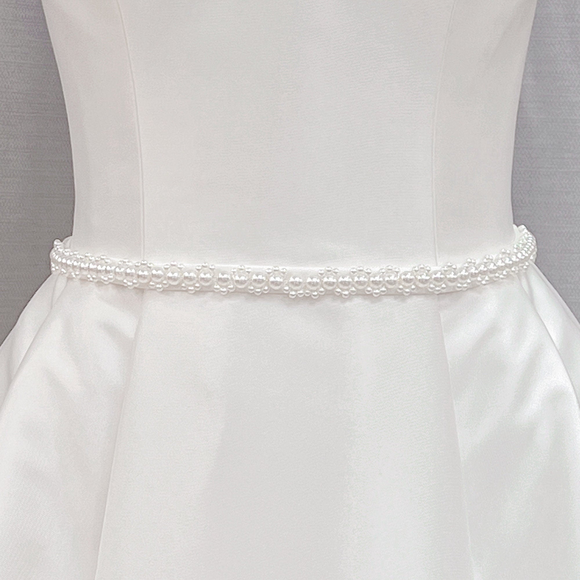 Minimalist pearl bridal belt with delicate white pearls displayed on a white bridal gown fabric background.