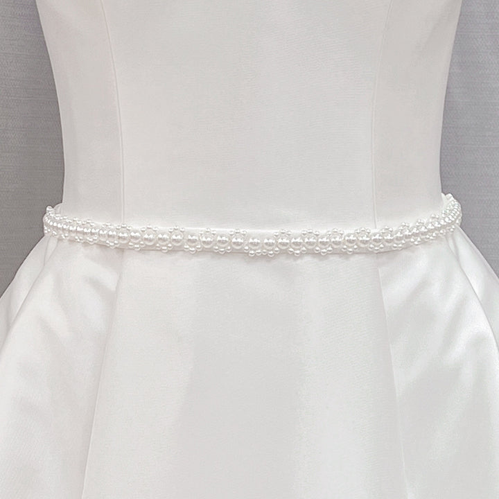 Minimalist pearl bridal belt with delicate white pearls displayed on a white bridal gown fabric background.