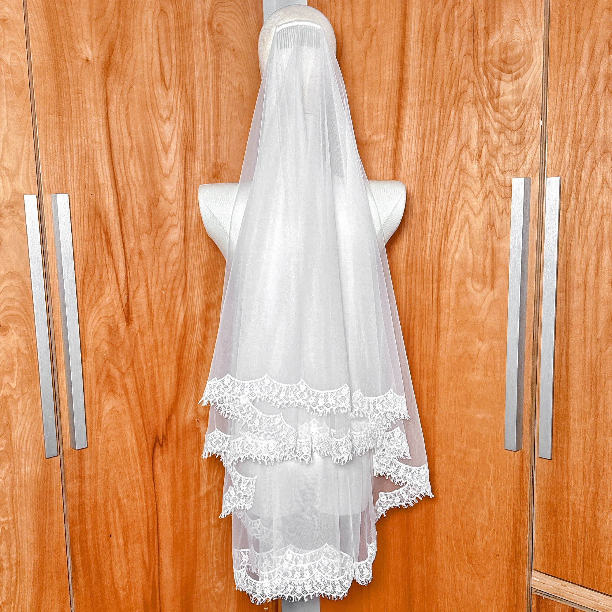 Modern hip-length drop wedding veil featuring a wide lace trim, photographed on a mannequin for a minimalist bridal look.