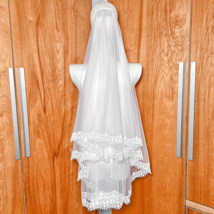 Modern hip-length drop wedding veil featuring a wide lace trim, photographed on a mannequin for a minimalist bridal look.