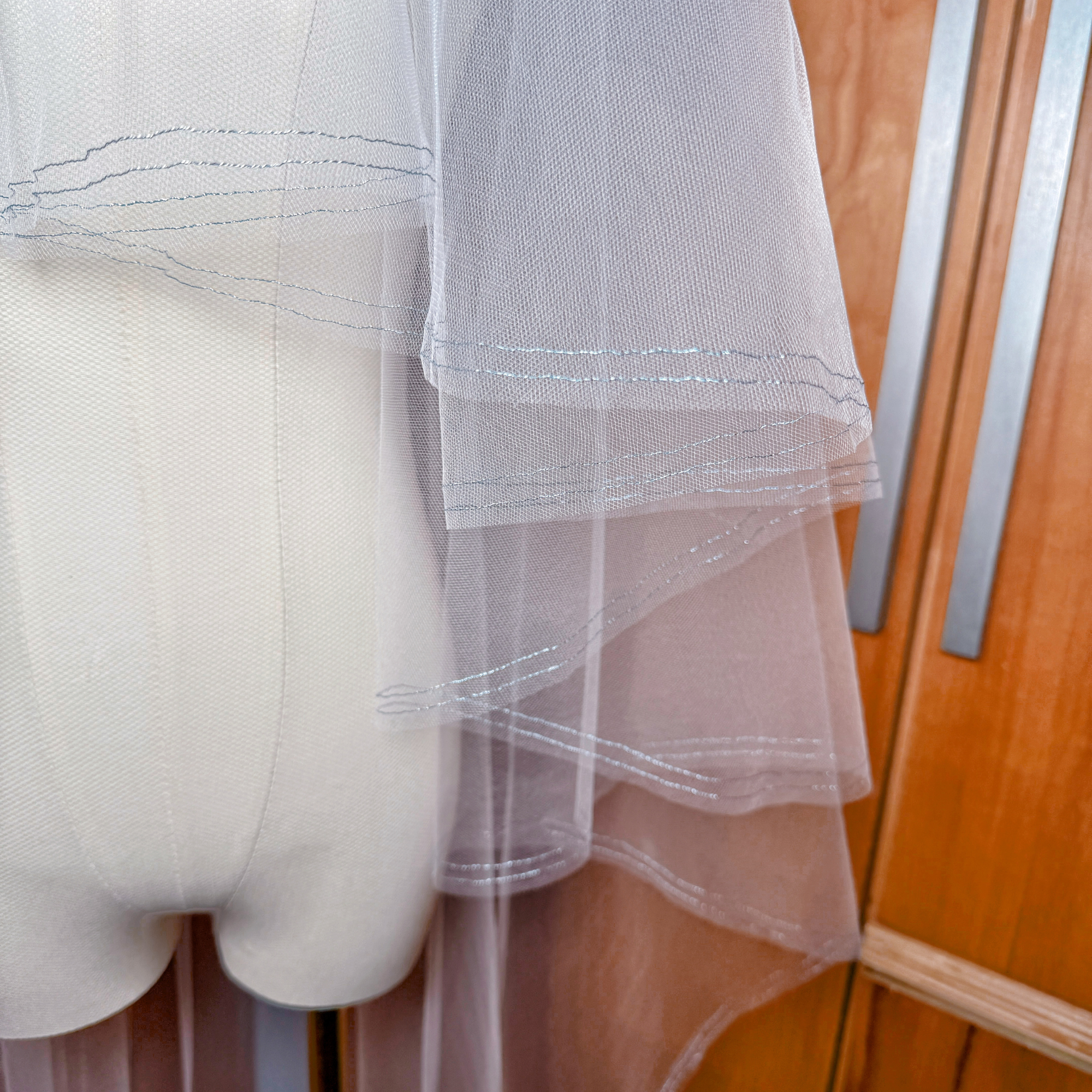 Waltz length bridal veil featuring two tiers, a front blusher, and a unique metallic blue finished edge.