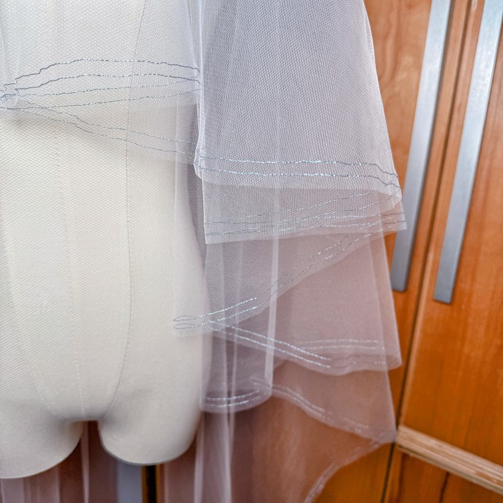 Waltz length bridal veil featuring two tiers, a front blusher, and a unique metallic blue finished edge.