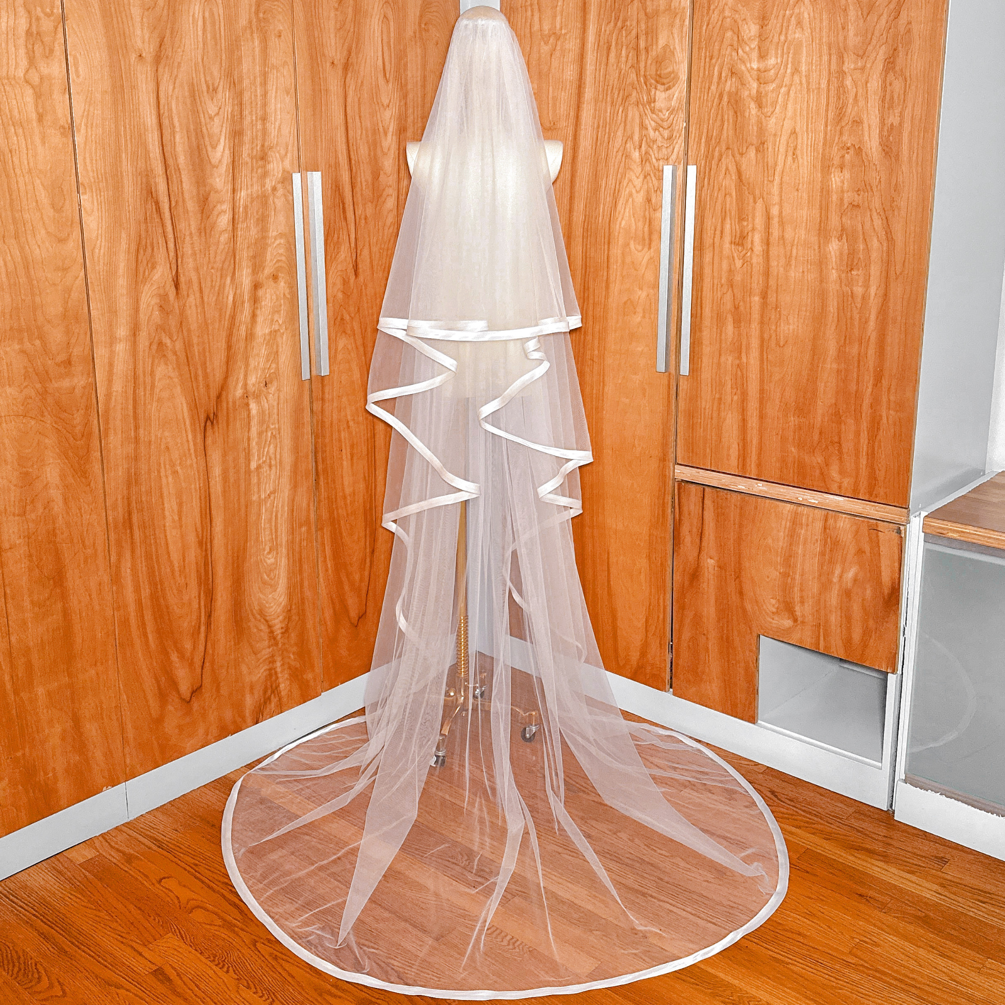 A bridal mannequin wearing a cathedral length veil finished with a 1 inch wide ribbon edge.