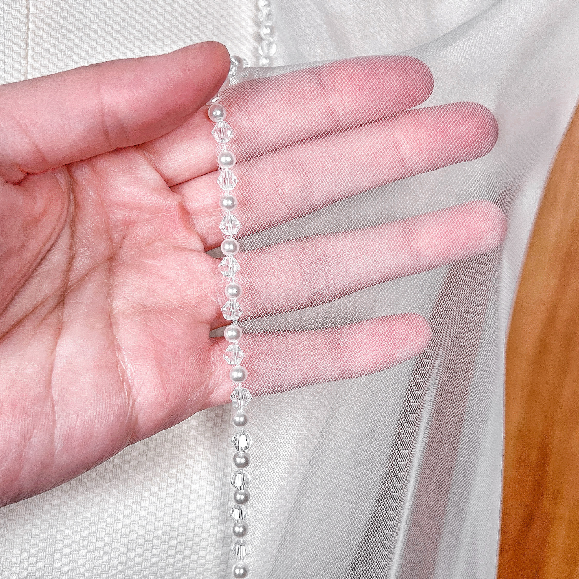 Close-up of the intricately hand-beaded edge on a fingertip wedding veil with alternating pearls and crystals.
