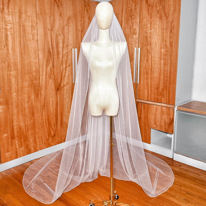 A long cathedral length wedding veil featuring a delicate hand-beaded edge with shimmering crystals and pearls.