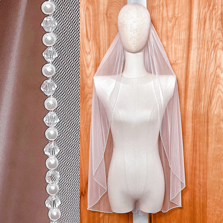Front view of a sheer fingertip length wedding veil featuring a delicate pearl and crystal beaded edge.