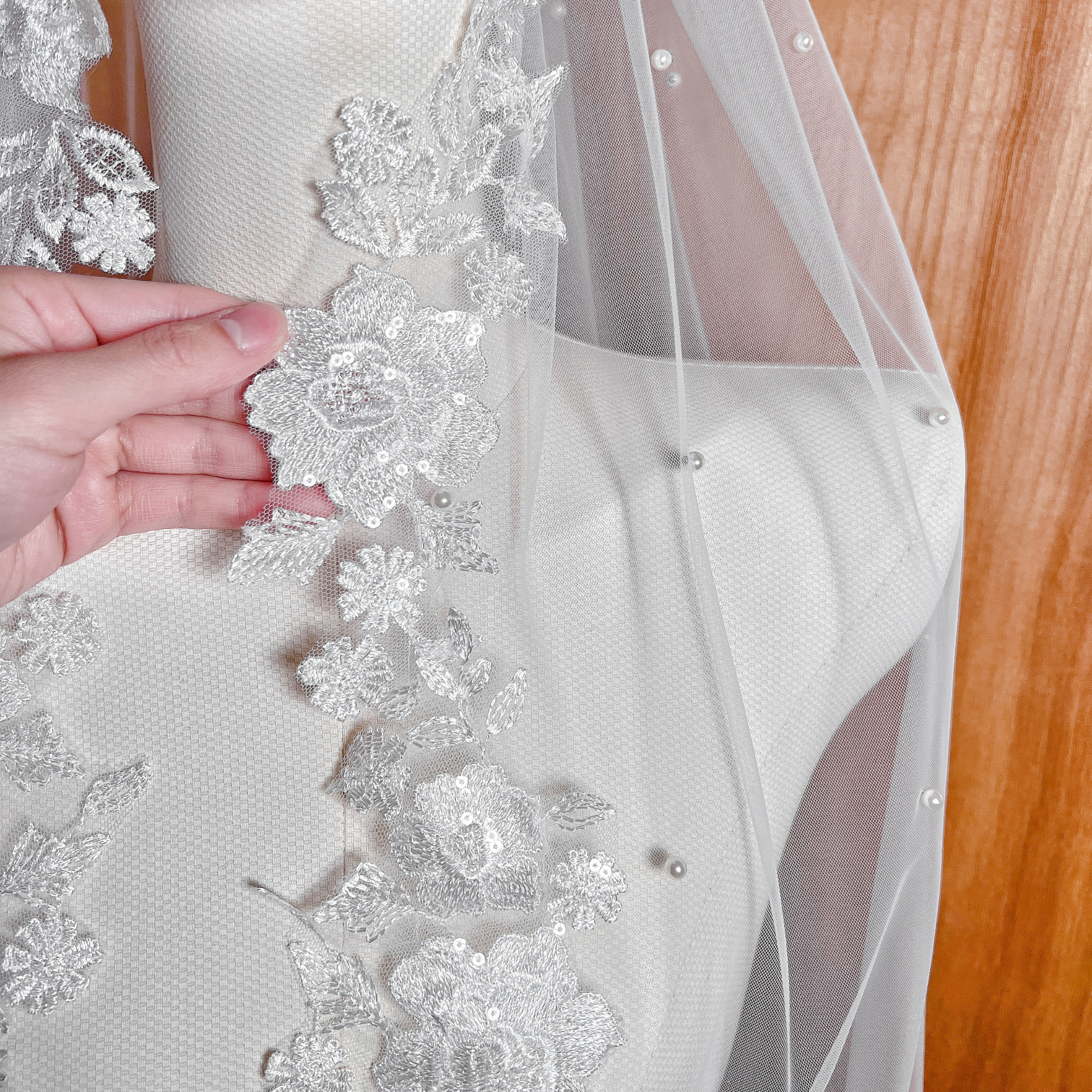 Close-up of a fingertip-length pearl and lace wedding veil on a mannequin, highlighting the intricate floral lace embroidery and scattered pearl accents.