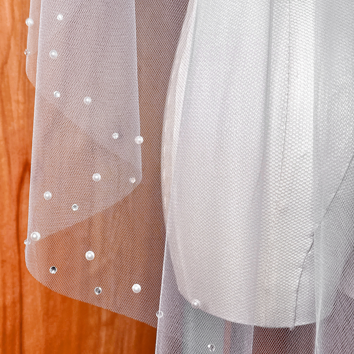 A close-up view of a fingertip length wedding veil adorned with delicate pearls and shimmering rhinestones, shown on a display bust.