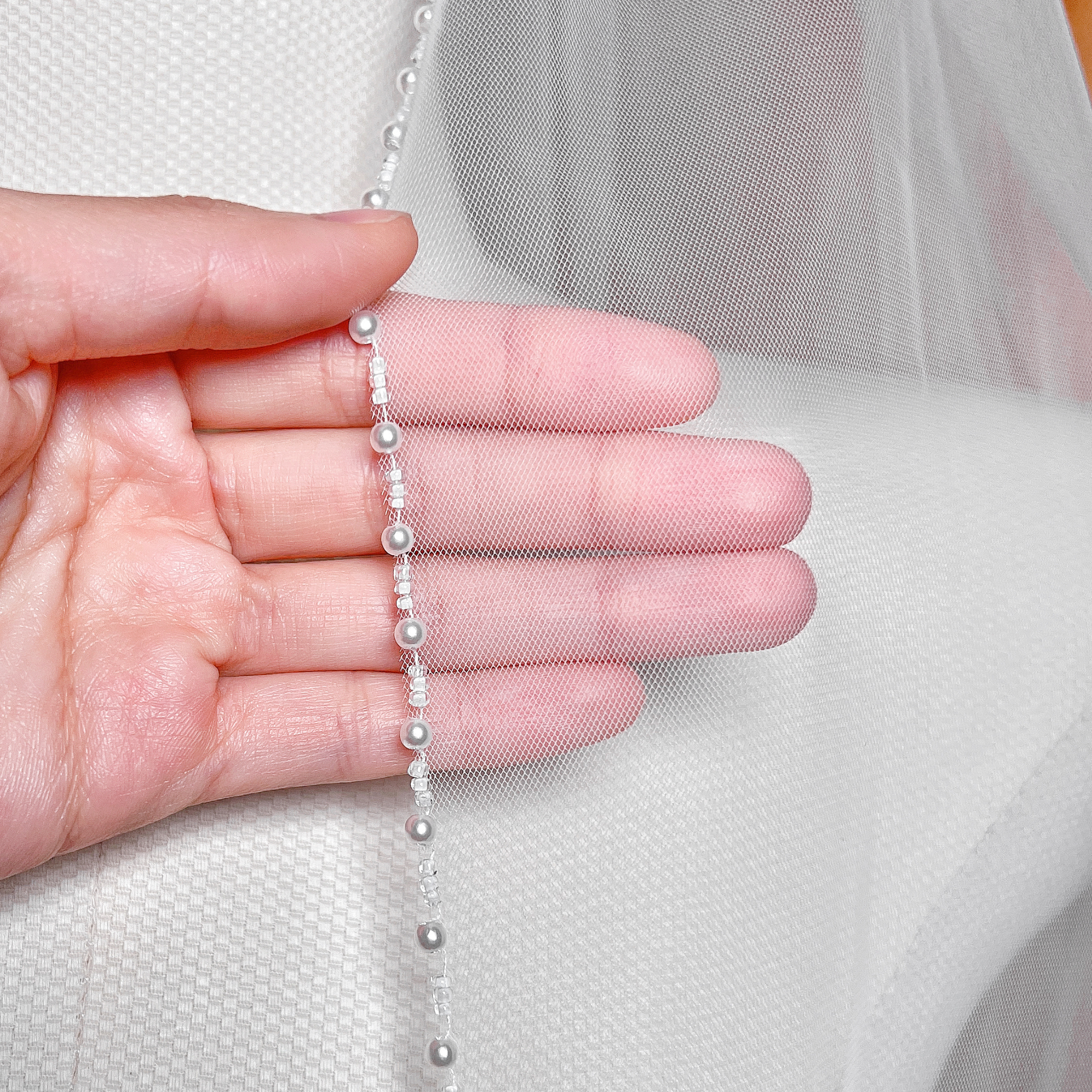 Close-up of shimmering ivory pearls and fine beadwork along the edge of a soft tulle wedding veil.