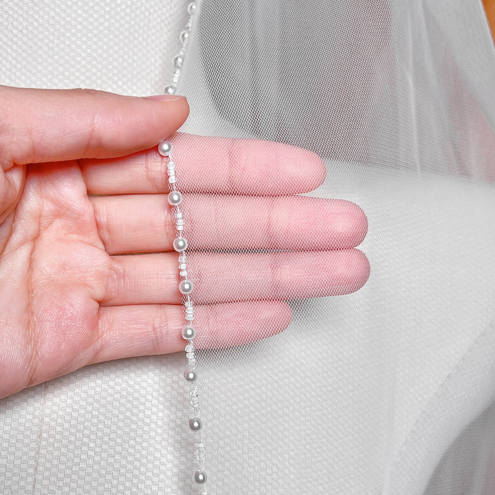 Close-up of shimmering ivory pearls and fine beadwork along the edge of a soft tulle wedding veil.