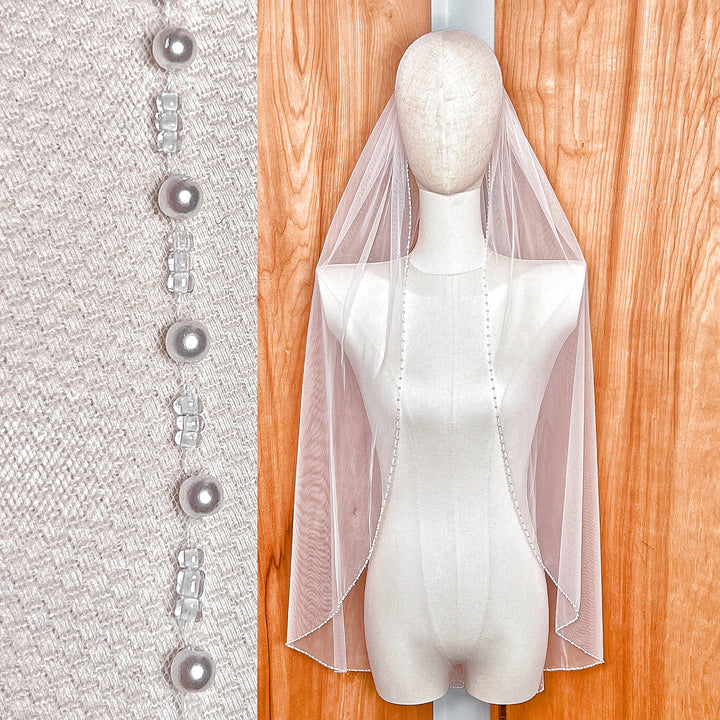 A single-tier, fingertip-length bridal veil with a delicate pearl beaded edge draped elegantly.