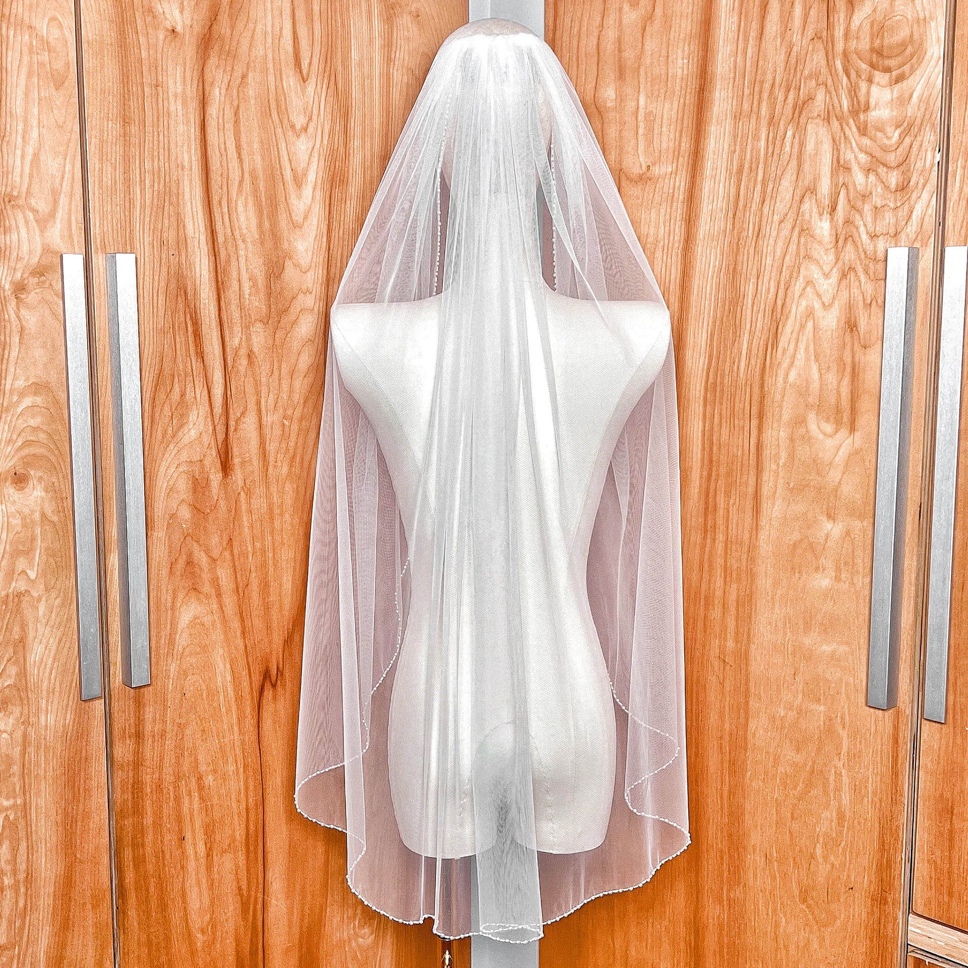 Back view of a fingertip-length wedding veil featuring a hand-sewn pearl beaded trim for a classic bridal look.
