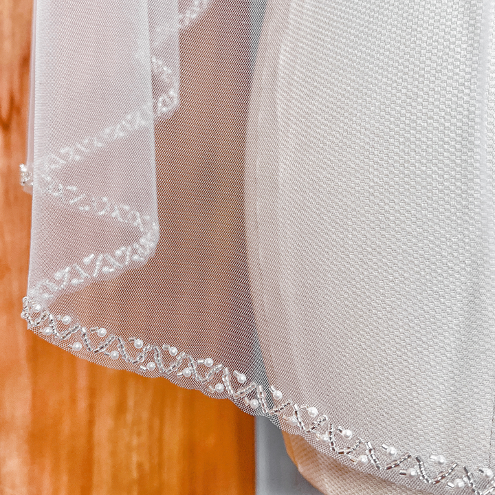 Ivory soft tulle wedding veil with a hand-stitched pearl beaded edge in a classic fingertip length.