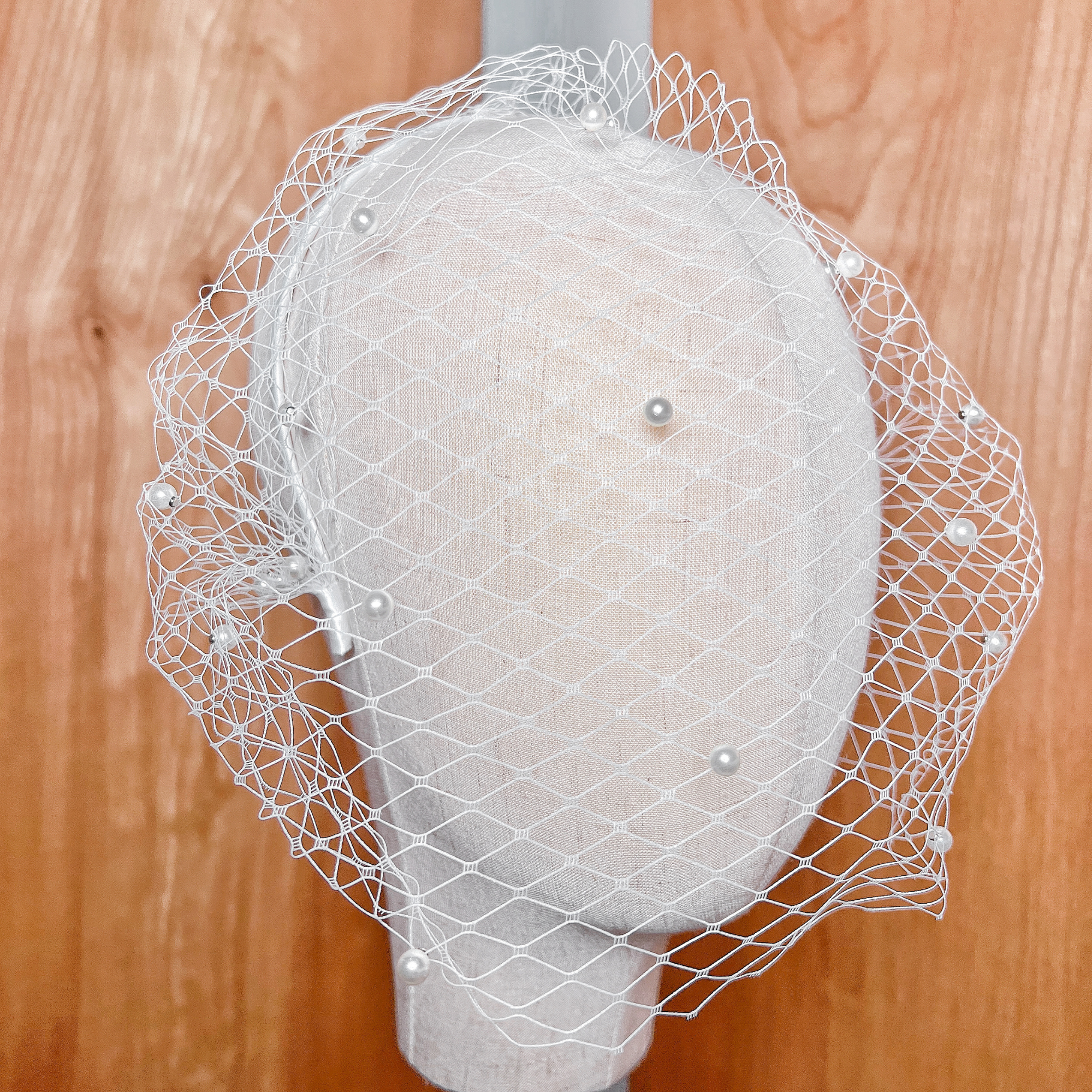 Close-up of a short white pearl birdcage wedding veil featuring scattered delicate pearls on textured netting.