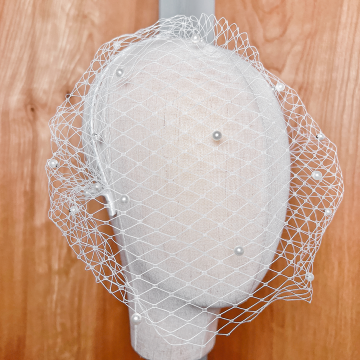 Close-up of a short white pearl birdcage wedding veil featuring scattered delicate pearls on textured netting.
