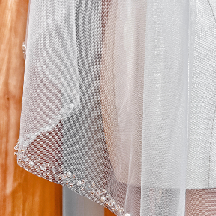 Fingertip length wedding veil with a detailed pearl and crystal beaded edge displayed on a bridal mannequin.
