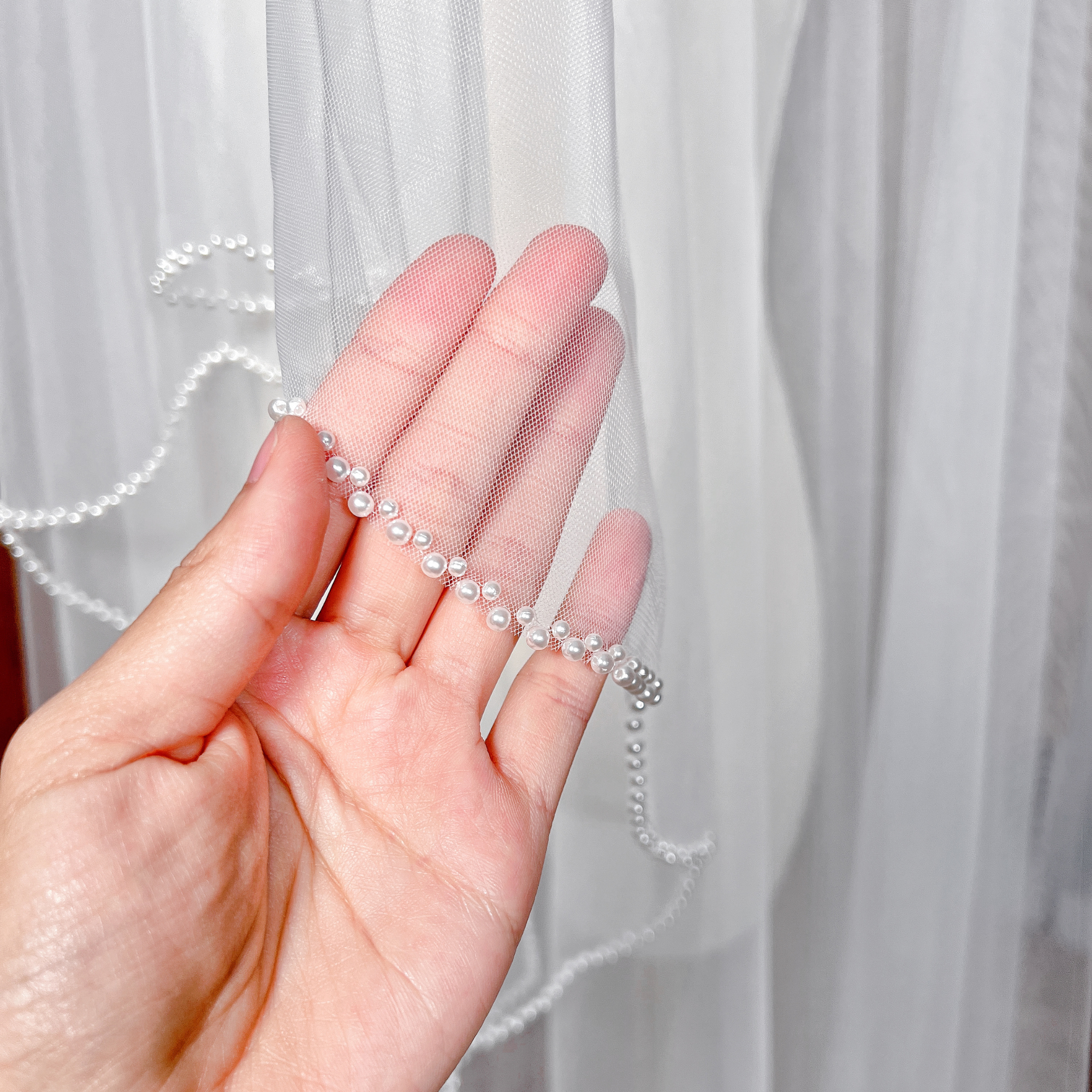Detail view of a two-tier cathedral bridal veil with pearl beaded edges and a front-facing blusher.