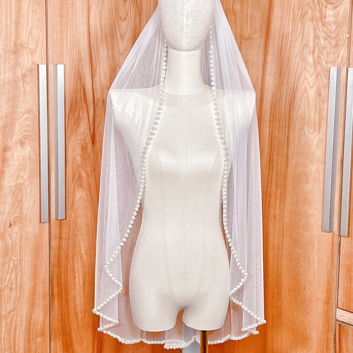 Side profile of a hip-length bridal veil illustrating the elegant drape and pearl-beaded border.