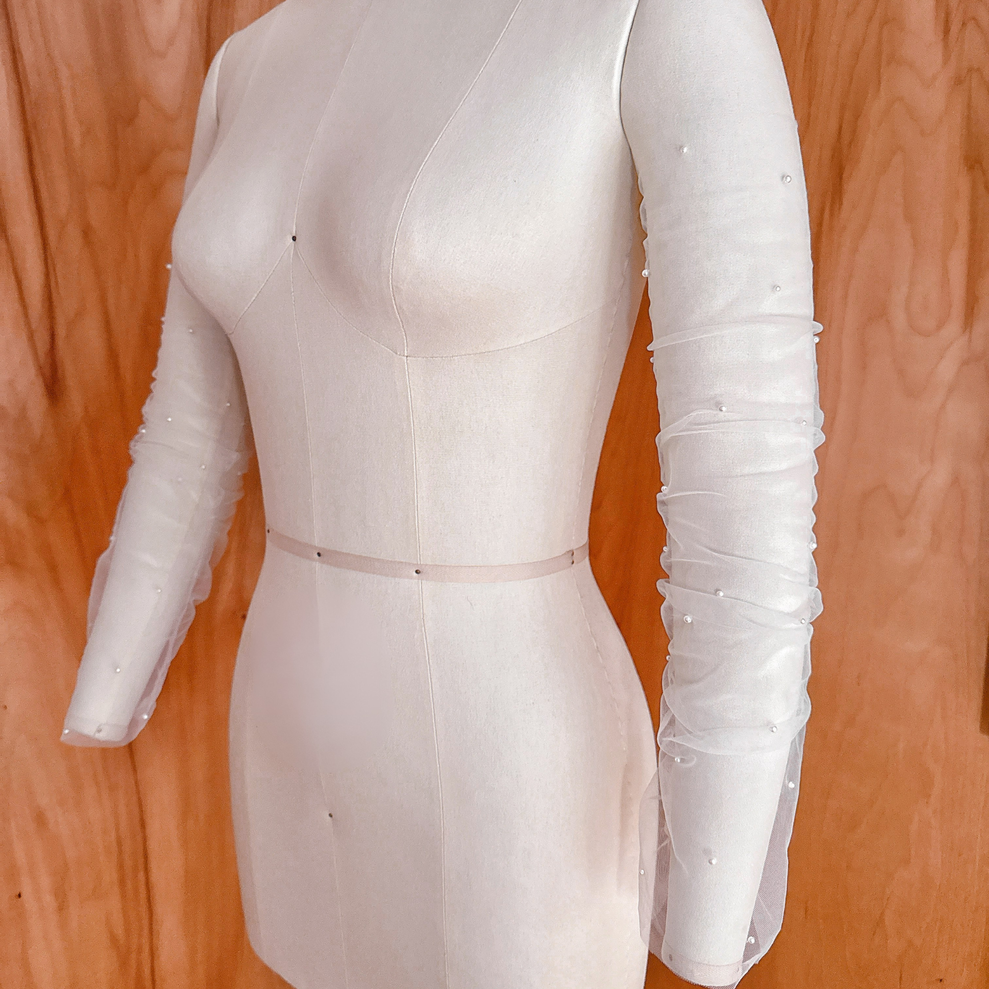 A side-angle studio shot of the pearl-scattered ruched tulle bridal sleeves on a mannequin, showcasing the drape and volume along the length of the arm.