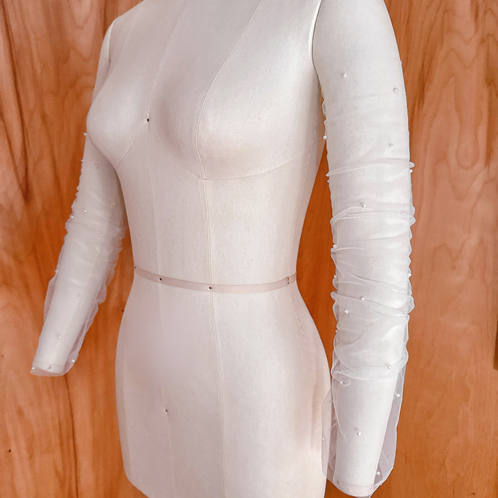A side-angle studio shot of the pearl-scattered ruched tulle bridal sleeves on a mannequin, showcasing the drape and volume along the length of the arm.