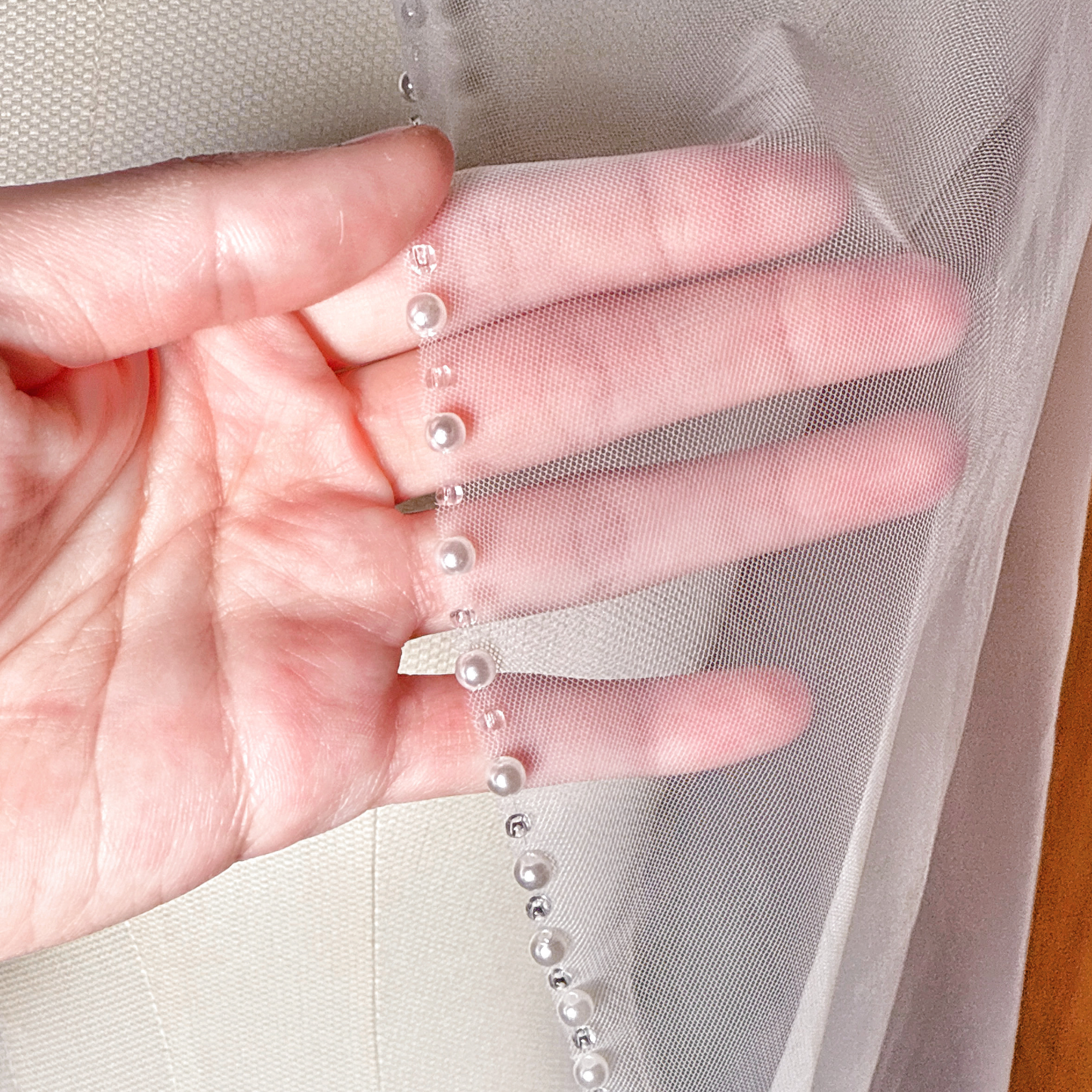 Close-up detail of the pearl lined edge on an ivory fingertip length wedding veil.