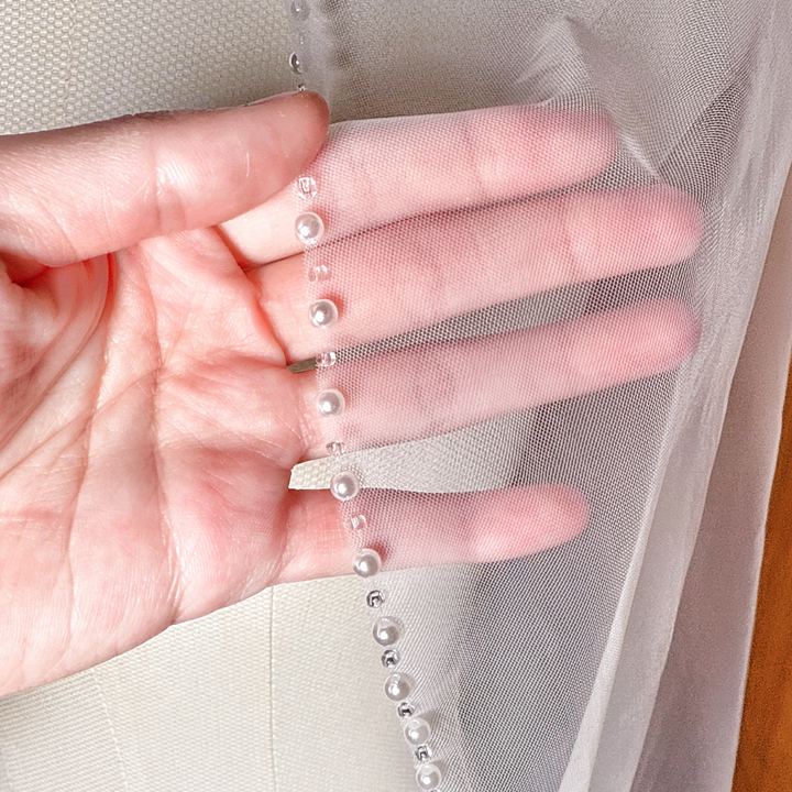 Close-up detail of the pearl lined edge on an ivory fingertip length wedding veil.