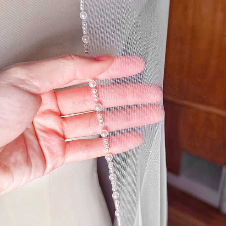 Close-up detail of the hand-beaded pearl trim on a cathedral length wedding veil, highlighting the lustrous pearls and sheer bridal tulle.