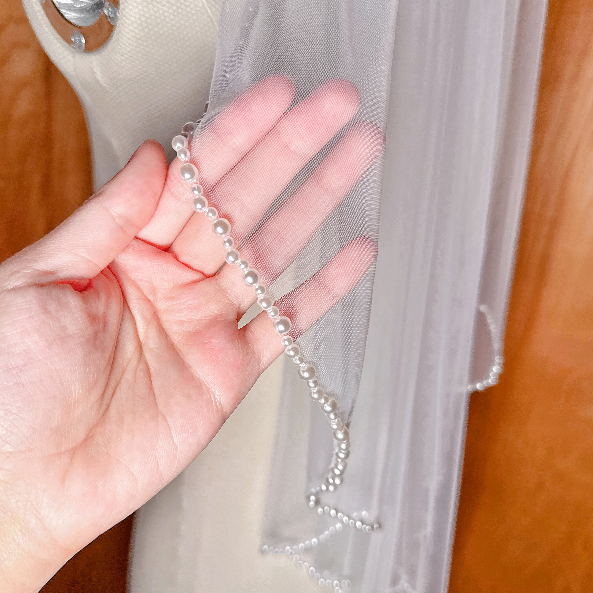 A close-up view of the delicate pearl trim along the edge of an elbow-length wedding veil, showing the intricate beadwork.