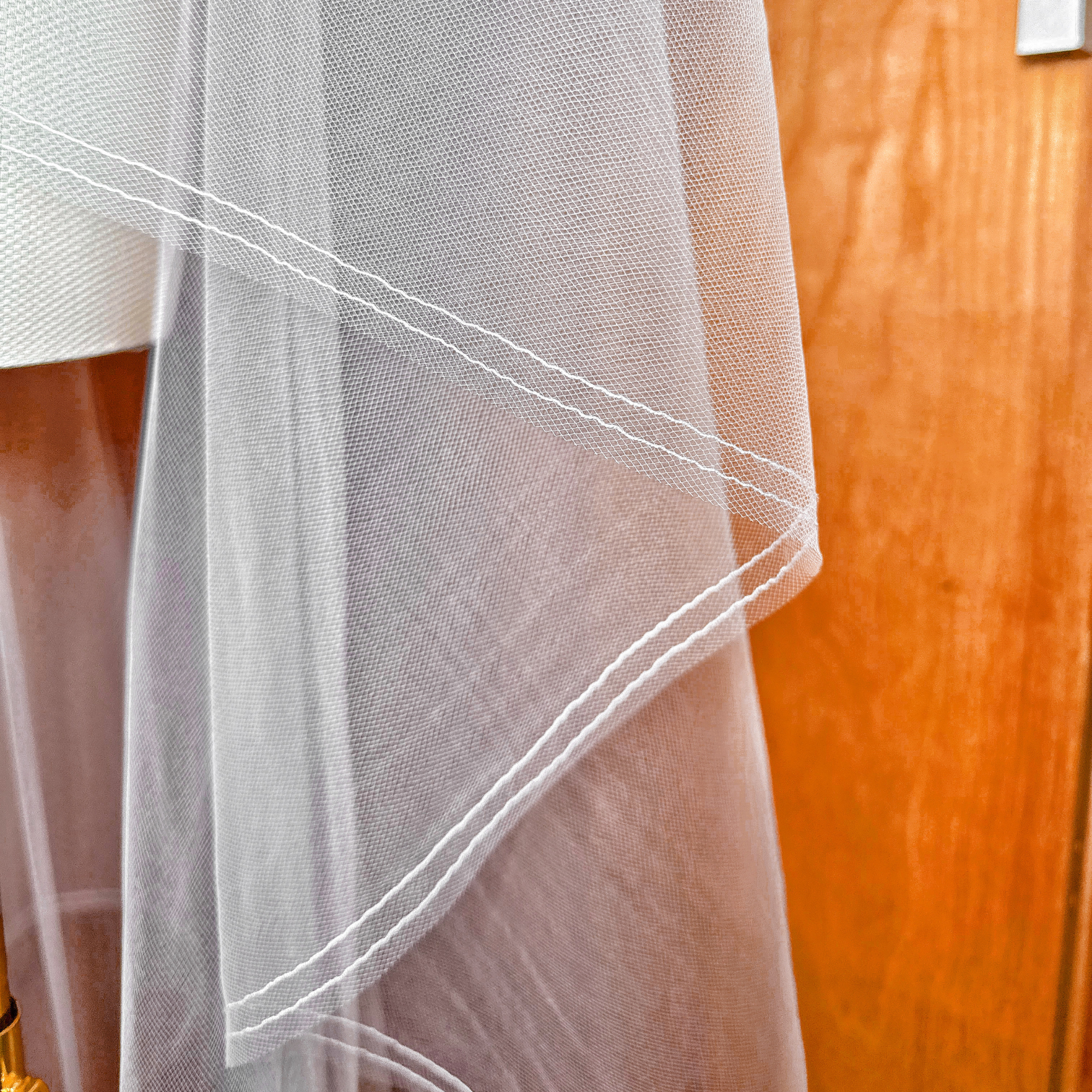 Close-up of the crisp pencil edge on a waltz length two tier wedding veil with blusher draped over a mannequin.