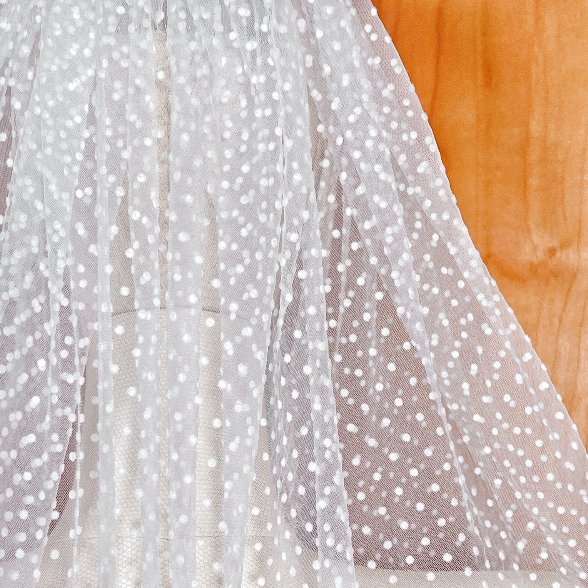 Close-up of the intricate polka dot texture and sheer ivory tulle of a fingertip-length bridal veil.