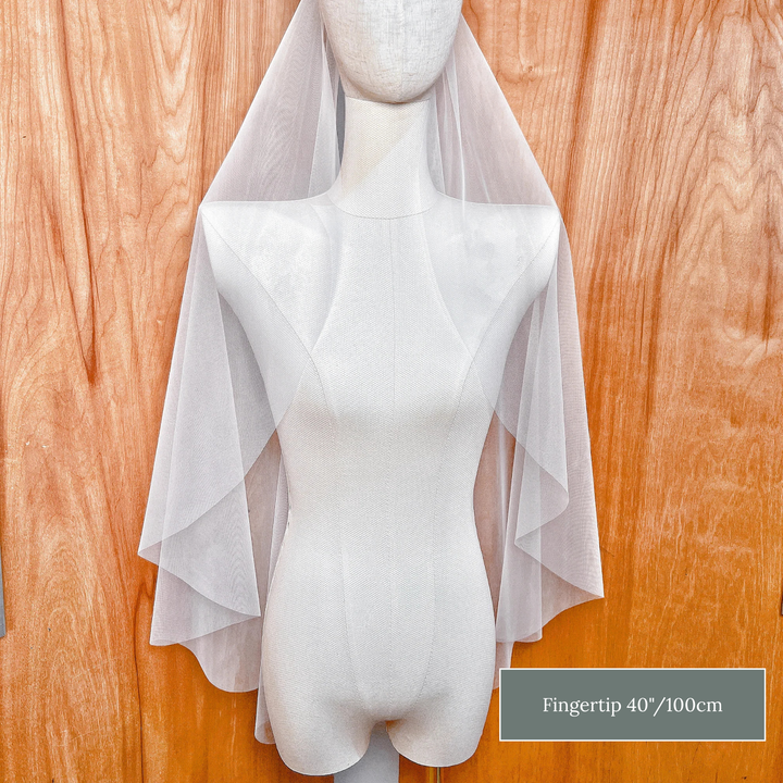 Sheer raw edge cascade wedding veil in fingertip length featuring soft waterfall folds.
