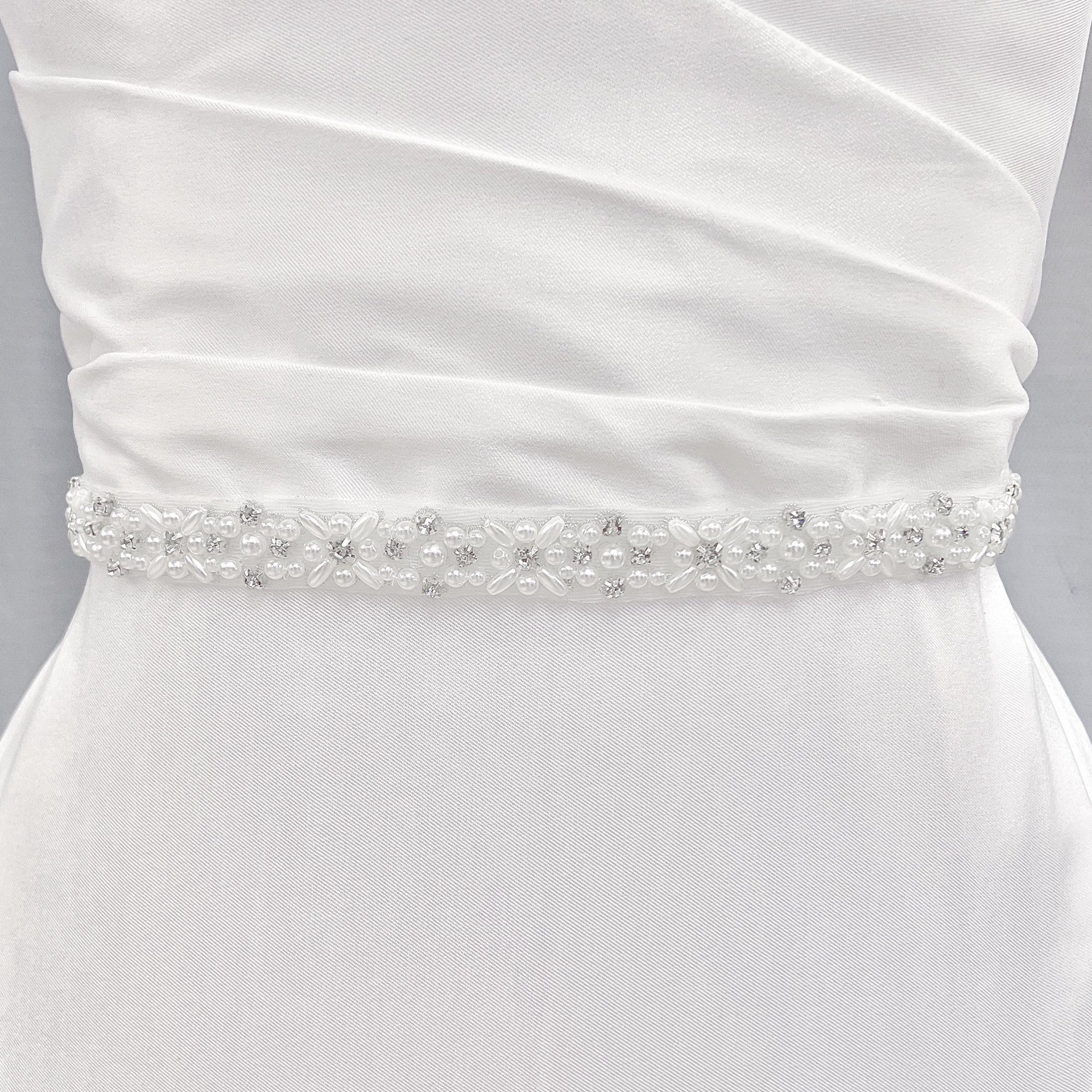 A sparkling rhinestone and pearl bridal belt displayed on a dress form mannequin.